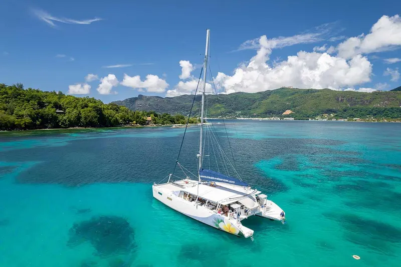 A motor yacht cruising past a lush tropical island in the Sainte Anne Marine National Park on a premium seychelles boat tour from Mahé